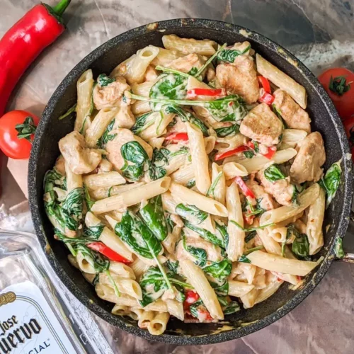 tequila chicken penne pasta in a pan with chili peppers on the side