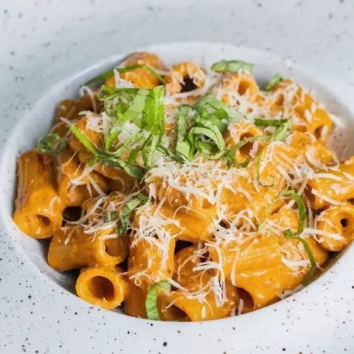Carbone's Spicy Rigatoni in a bowl with grated parmigiano reggiano and basil