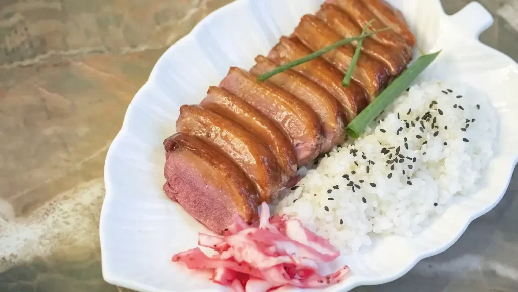 miso glazed duck breast on a plate with a side of white rice and pickled cabbage