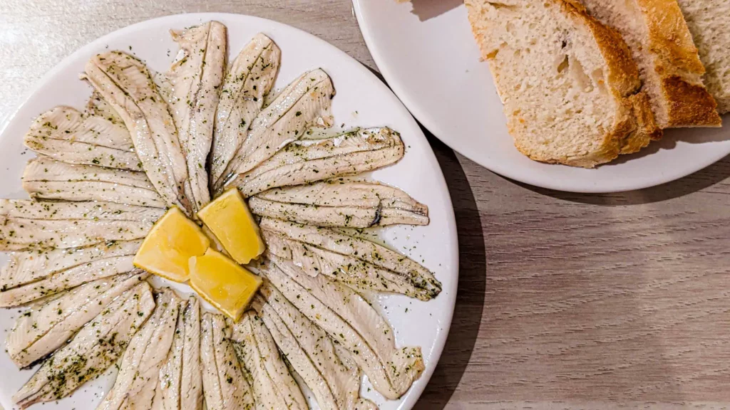 spanish marinated anchovies on a white plate with lemon wedges in the middle
