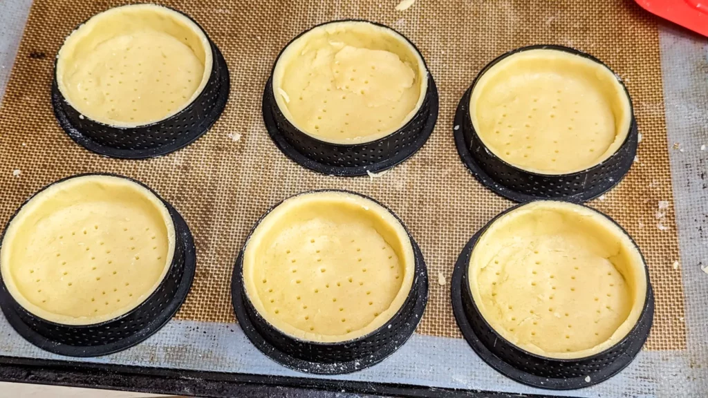 six tartelette shells in molds pre baking on a sheet pan