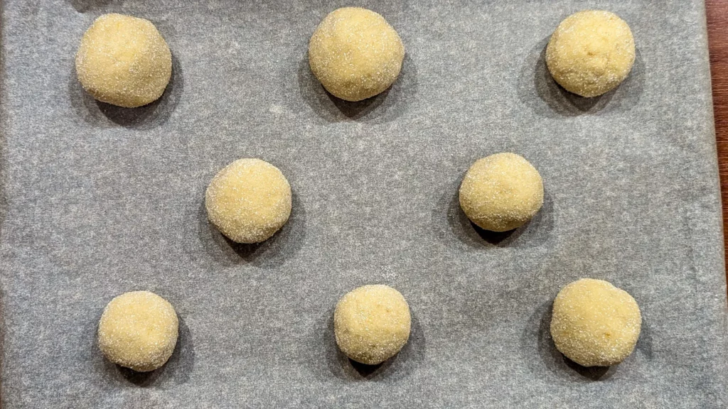 unbaked balls of lemon cookie dough rolled in sugar on a paper lined baking tray