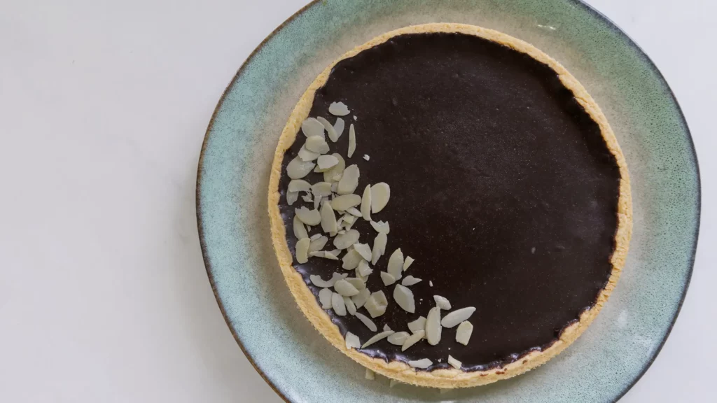 French style Chocolate Tart with almond sliver garnish on a ceramic plate