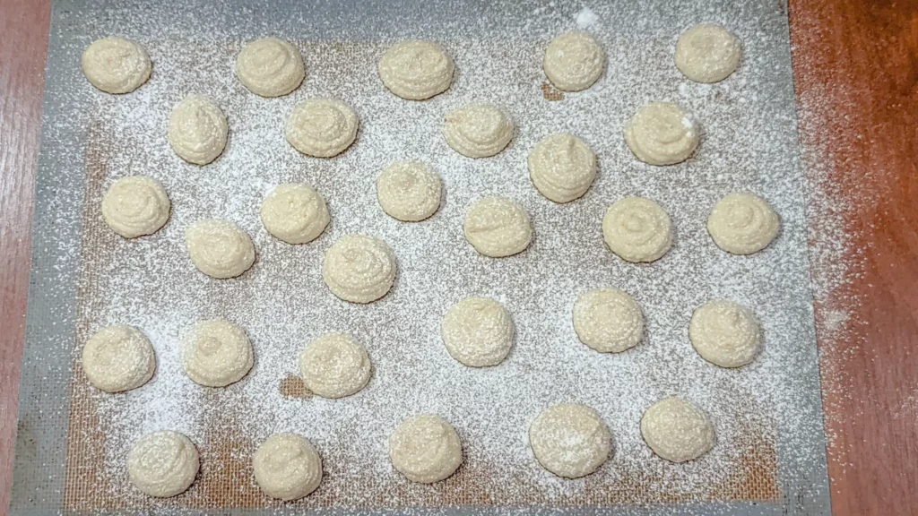 piped amaretti batter on a baking sheet with powdered sugar