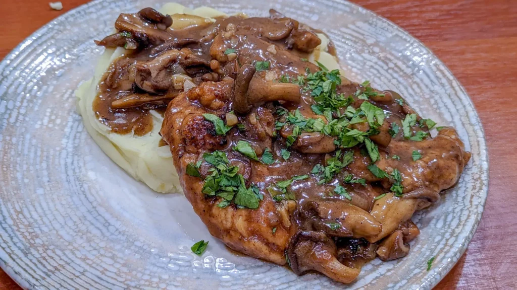 homemade chicken marsala with oyster mushrooms and parsley garnish. Laying on a bed of French whipped potatoes in a fancy plate