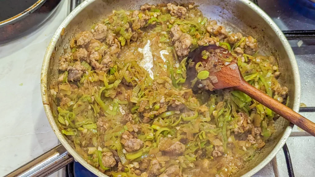 a reduced mix of onions, garlic, sausage, and leeks, in a steel pan with a wooden spoon