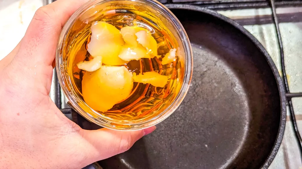holding a jar of bourbon and duck fat over a metal pan