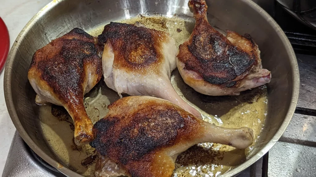four duck legs with crispy skin in a steel pan