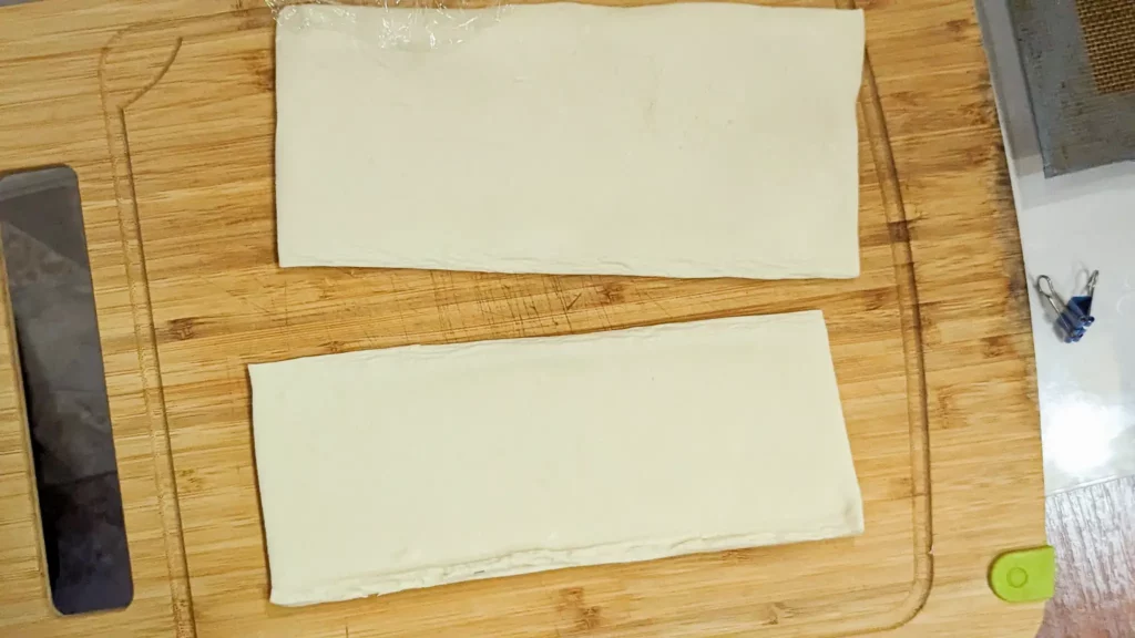 two strips of store bought puff pastry on a wooden cutting board