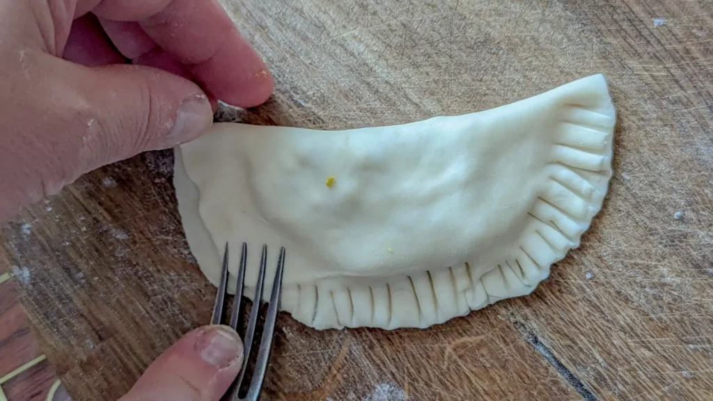 crimping chebureki dough shut with a fork on a wooden board