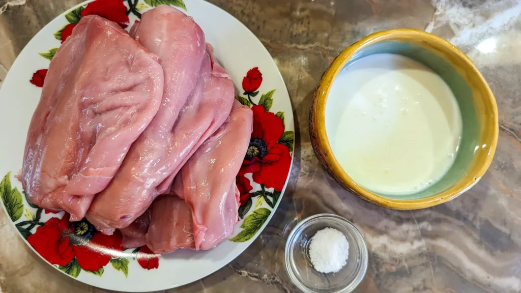 three rabbit loins on a plate next to a bowl of buttermilk and a little cup of salt