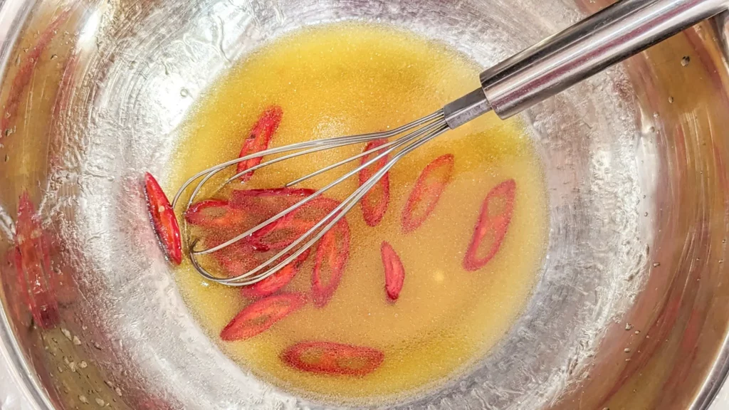 a metal bowl with citrus and chili dressing and a wire whisk