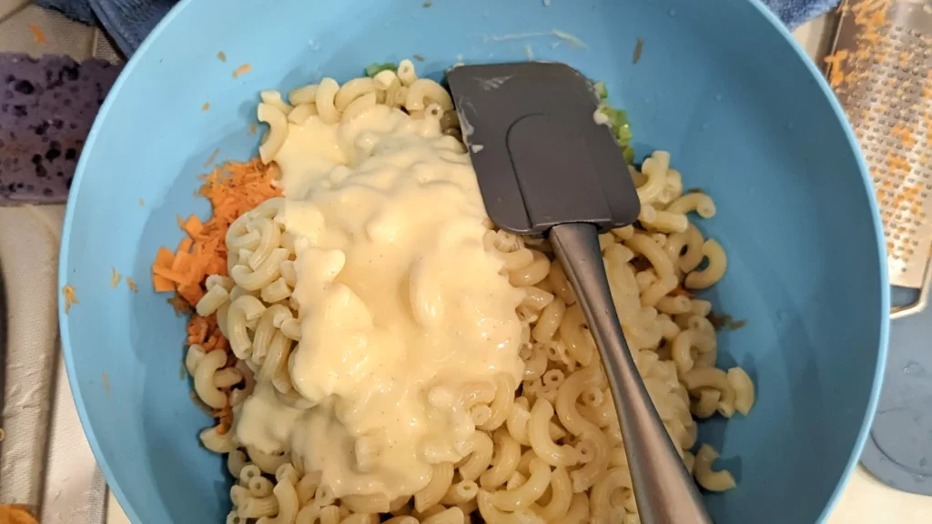 a large blue bowl with unmixed mac salad ingredients and a rubber spatula
