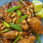 chili lime chicken wings on a blue plate with peanuts and lime wedges as a garnish
