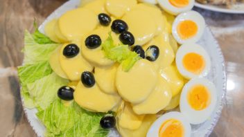 a plate of papa a la huancaina on a bed of lettuce with black olives an boiled eggs for garnish
