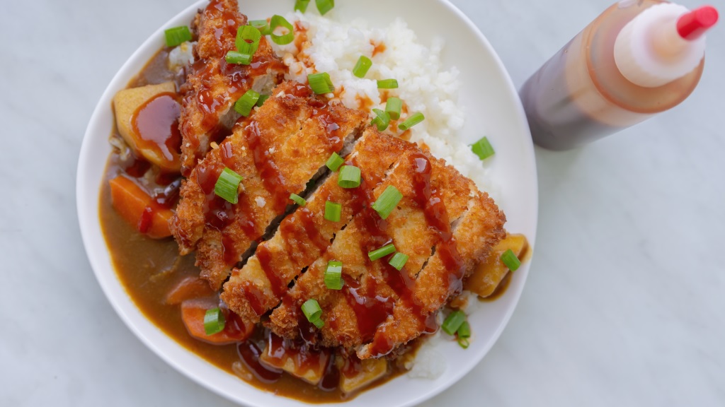 a plate of tonkatsu curry with white rice and a squeeze bottle of homemade bulldog sauce