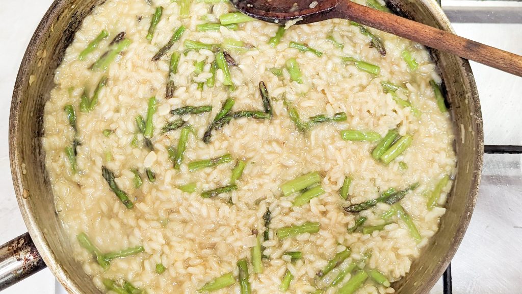 lemon asparagus risotto in a steel pan with a wooden spoon on a cooktop