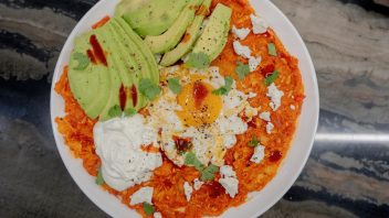 chilaquiles with egg and avocado and cheese and sour cream on a large white plate on a quartzite counter