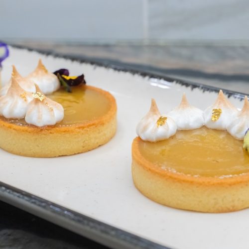 three gooseberry curd tarts on a serving dish with baked meringue and gold leaf garnish