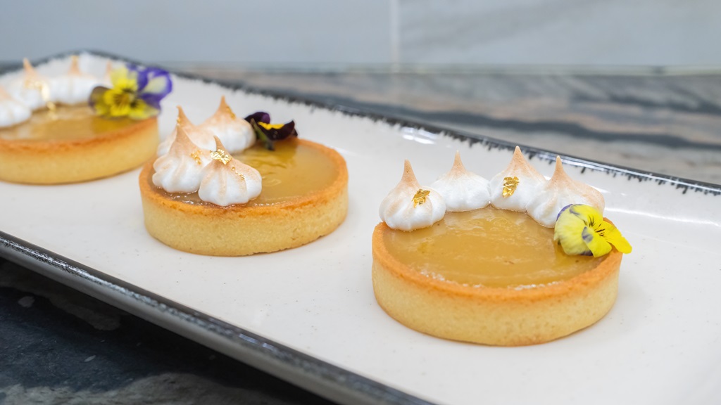 Three gooseberry curd tartlets with toasted meringue on a presentation dish
